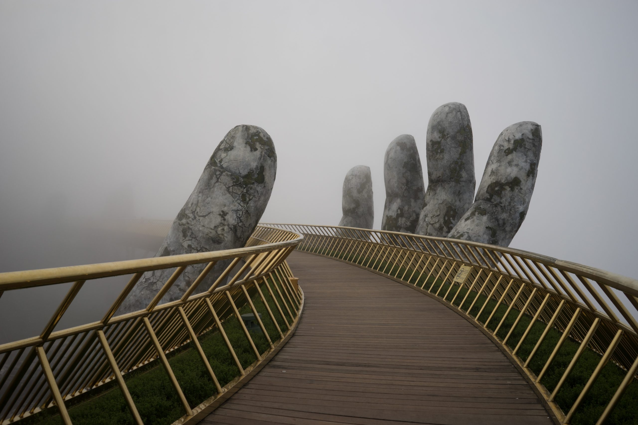 A footbridge in the fog. The bridge is held up by a concrete hand.