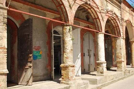 A street scene in Jakmèl, Ayiti. (also known as Jacmel, Haiti) A colonnade with several open bays.