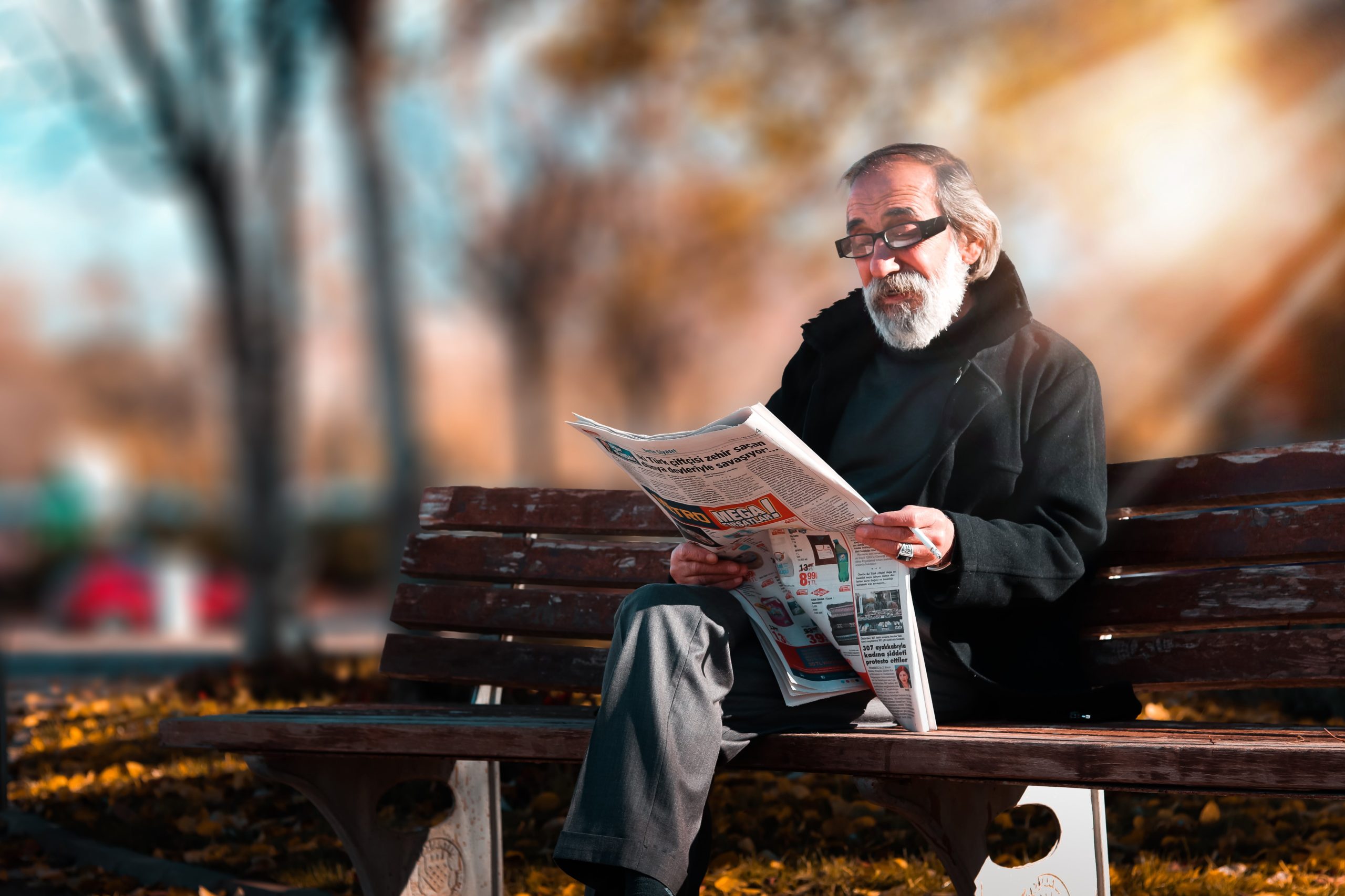 Man sitting on a park bench reading a newspaper