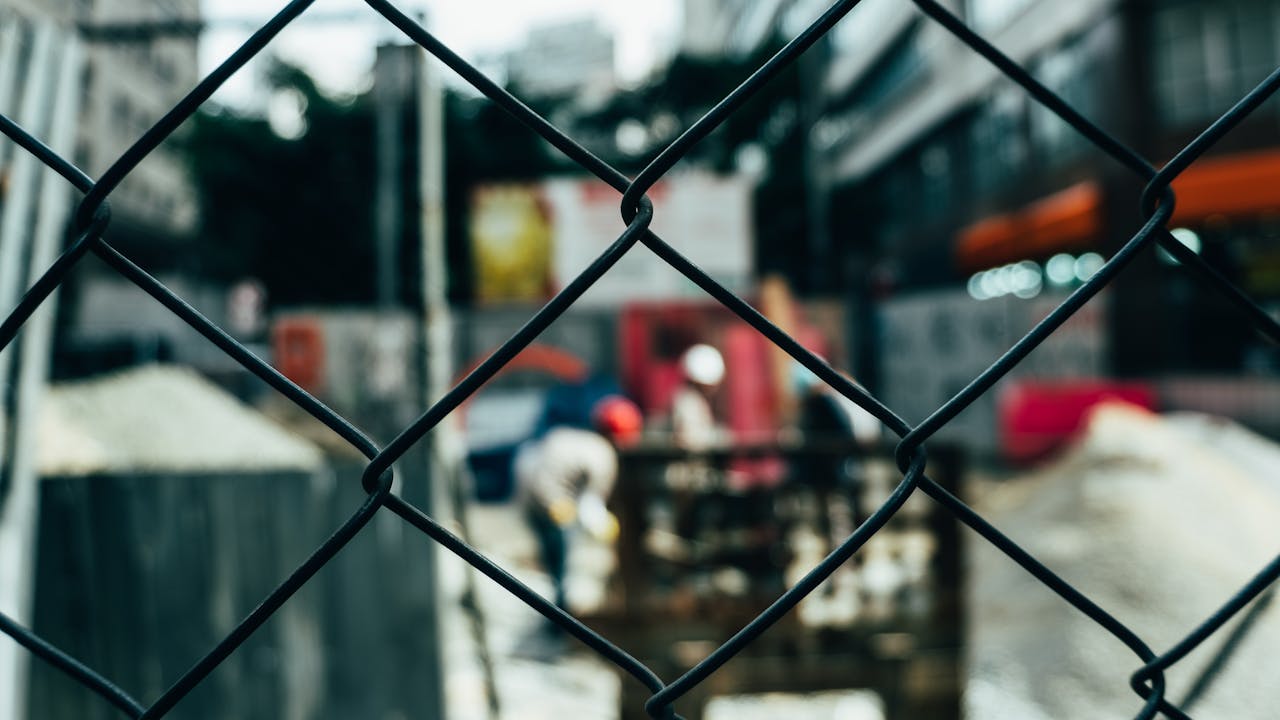 a blurred city neighborhood behind a black chain link fence.