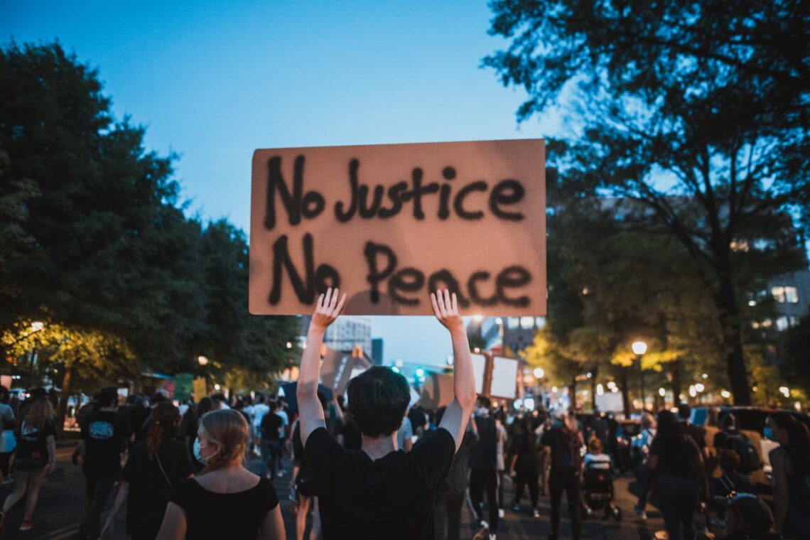 A man at a protest holds a sign reading "No Justice, No Peace."