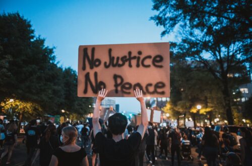 A man at a protest holds a sign reading "No Justice, No Peace."