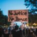 A man at a protest holds a sign reading "No Justice, No Peace."