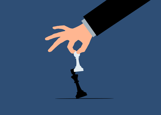A hand reaches down to take a white chessboard pawn to knock over a black king against a blue background